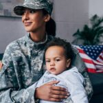 african american female soldier in military uniform with baby boy at home, with american flag on