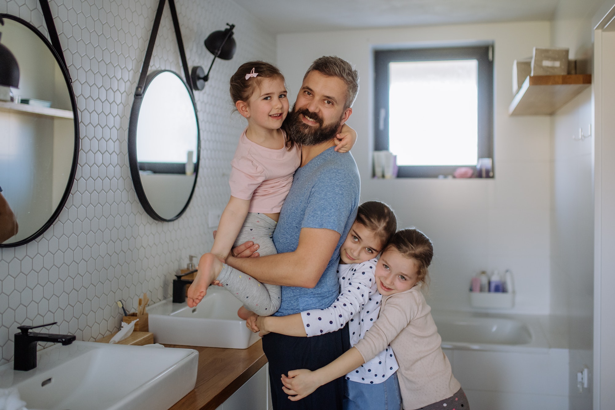 Father bonding with his three little daughters in bathroom and looking at camera.